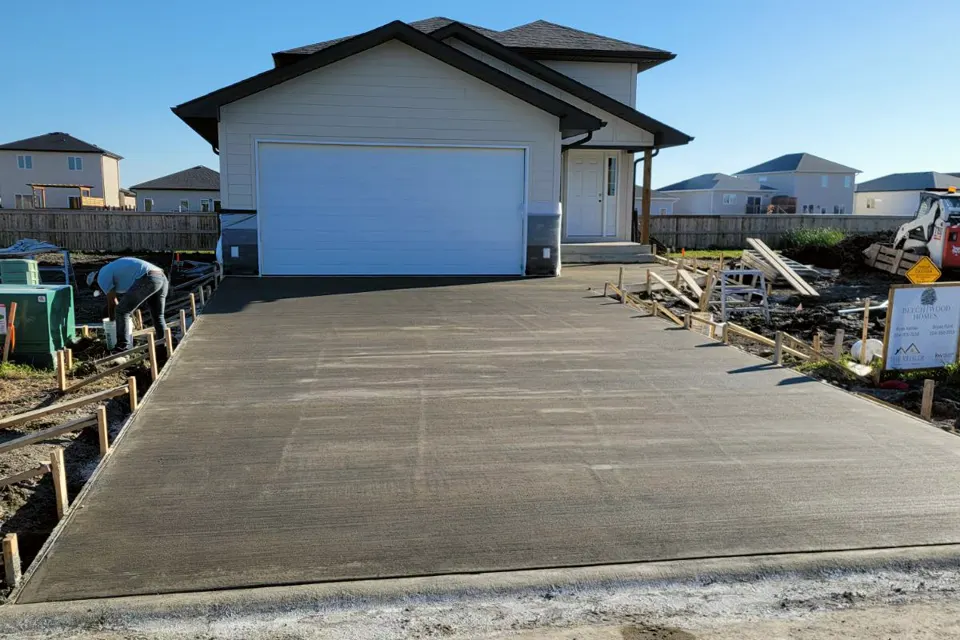 Real job-site photo of a new home with a double garage and a freshly poured concrete driveway, with forms still along the edges