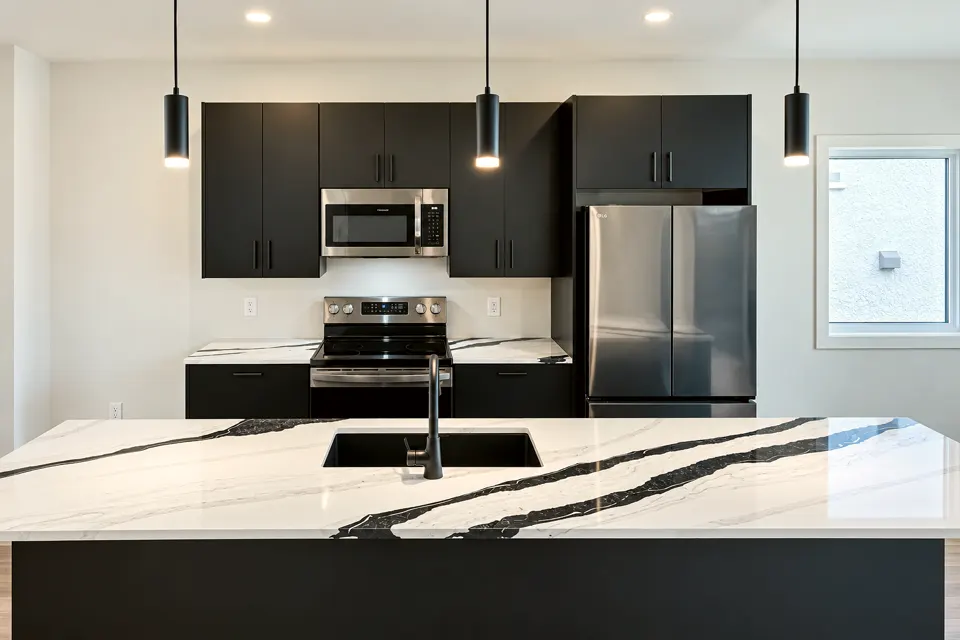 Kitchen with dark flat-panel cabinets, black pendant lights, a stainless fridge and a white island counter with dark veining