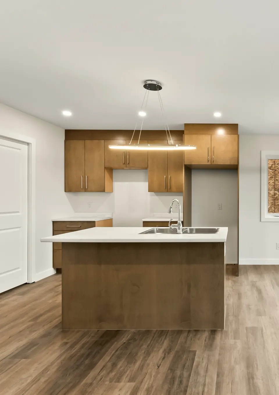 Kitchen island with a double sink, maple-tone cabinets and a linear pendant light