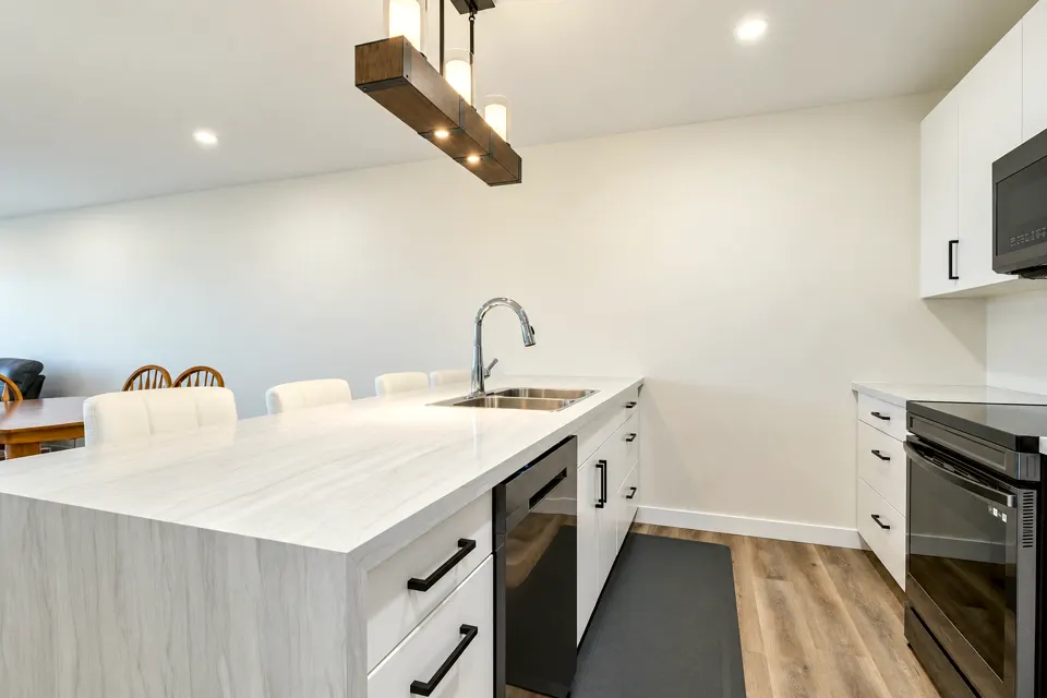 Kitchen with white flat-panel cabinets, black handles, a light waterfall-edge island and a wood-beam pendant light