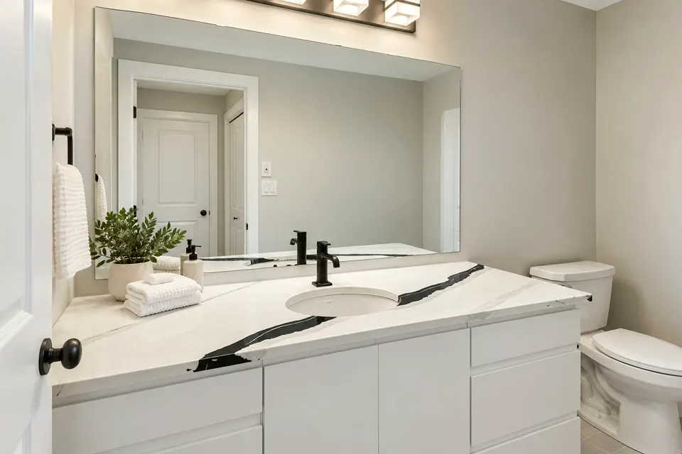 Bathroom vanity with a white cabinet, a veined counter, black fixtures and a large mirror